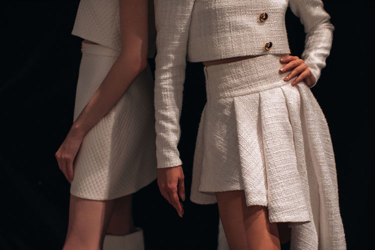 Two cropped female fashion figures in white stylish outfits on backstage