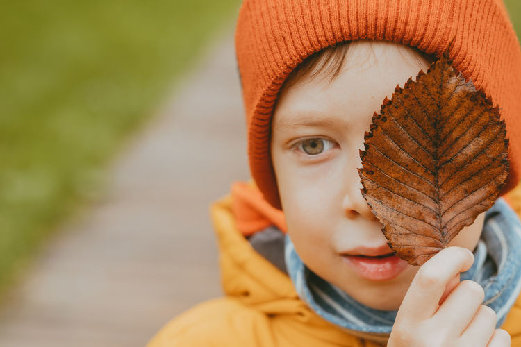 Boy with a withered leaf on his face in the fall. autumn theme. a dried autumn leaf in the hands