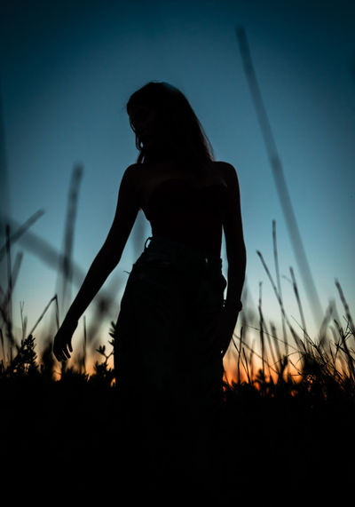Silhouette woman standing on field against sky at sunset