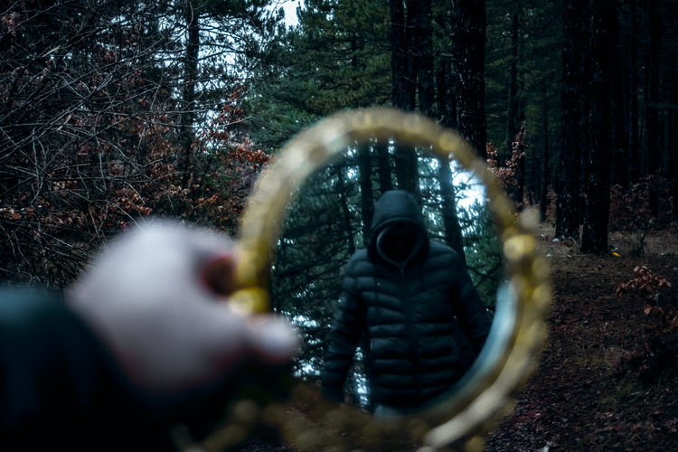 Reflection of person photographing through trees in forest