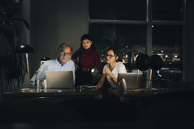 Senior businessman planning strategy with female colleagues at coworking space in dark