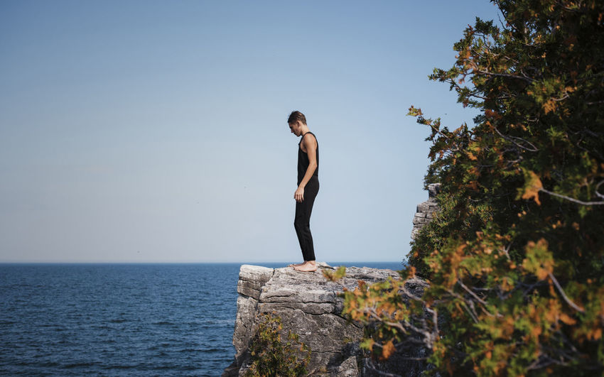 Full length of hiker standing on cliff against sea and clear sky at bruce peninsula national park