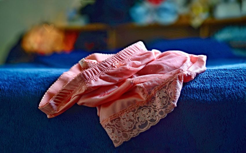 A pair of pretty pink panties, on the corner of a bed.