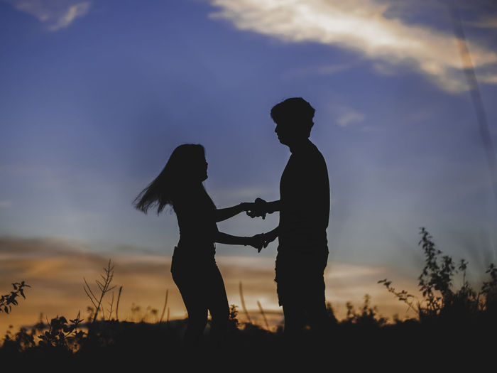 Silhouette couple standing on land against sky during sunset