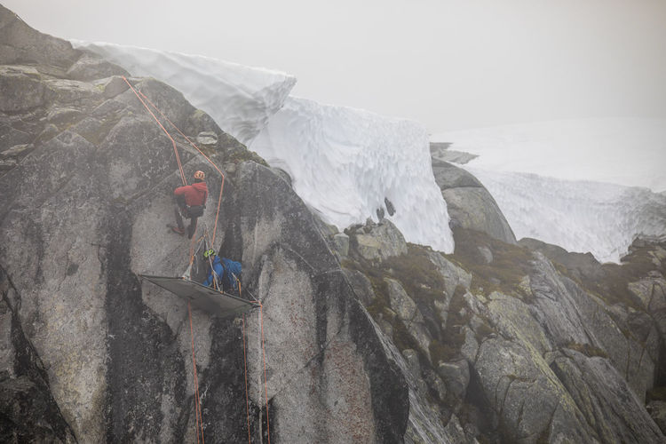 Climbers use rope to rappel onto portaledge on rock wall.