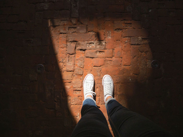 Woman in white sneakers stands in sun beam on old pavement made of red bricks.  light and shadow.