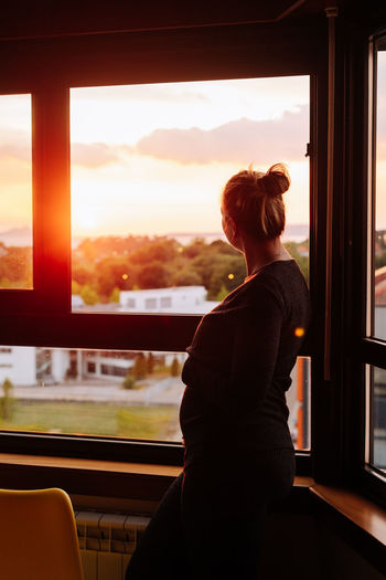 Pregnant woman of four months contemplating the sunset from the window of her flat