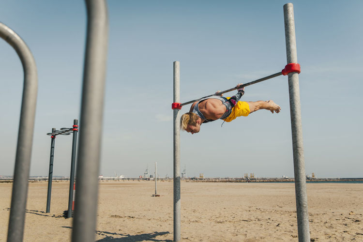 Male gymnastic exercising on high bar at beach