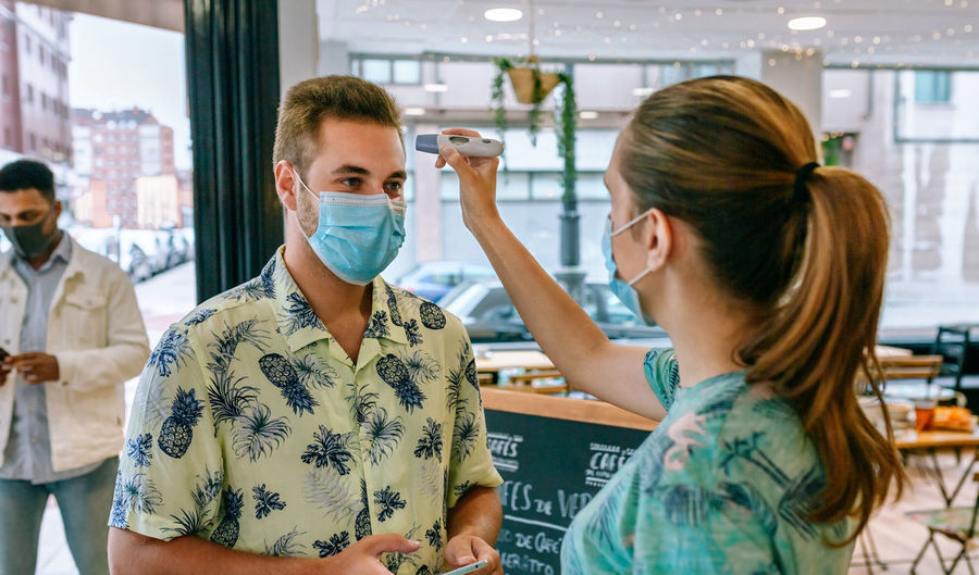 Woman checking temperature of customers wearing mask in restaurant