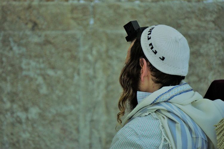 Rear view of man wearing hat and tefillin against wall