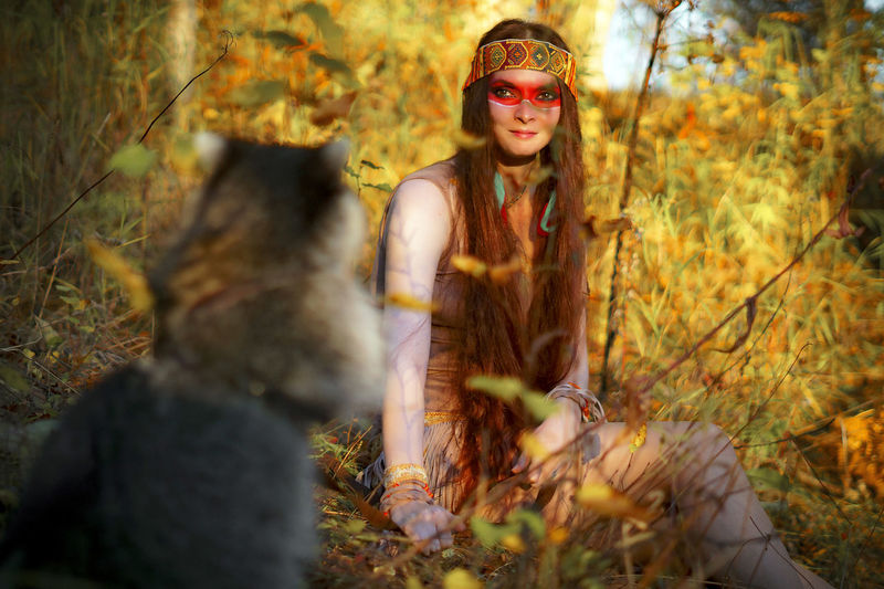 Young woman looking at raccoon while sitting in forest