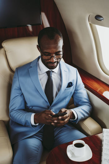 Young male entrepreneur text messaging on mobile phone in private jet