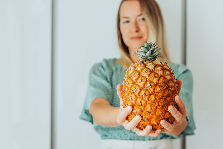 Young blond woman holding a pineapple in front of her
