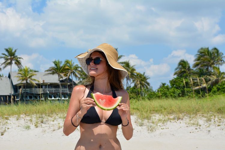 Young woman holding watermelon while standing at beach