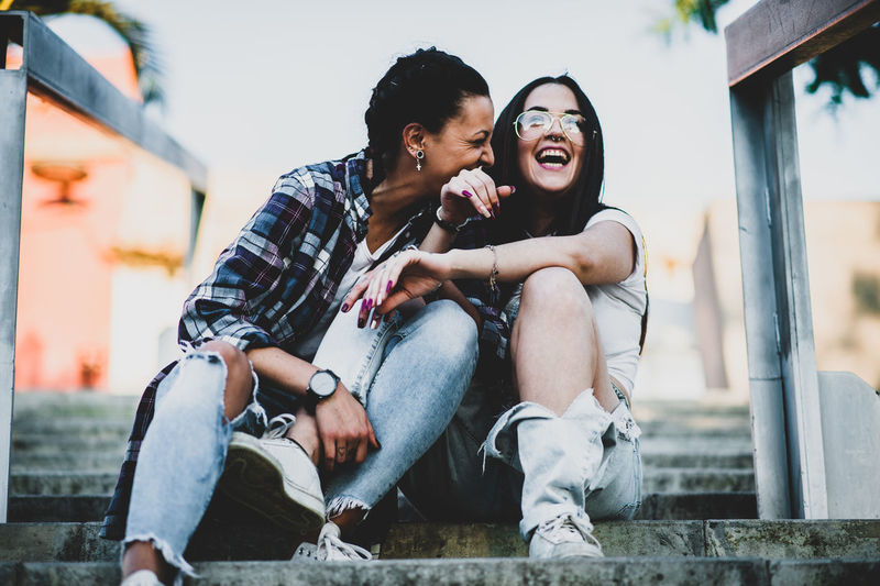 two women smiling sitted on a steps Architecture Bonding Building Exterior Built Structure Casual Clothing Couple - Relationship Emotion Full Length Happiness Leisure Activity Lifestyles Outdoors People Positive Emotion Real People Sitting Smiling Togetherness Two People Women Young Adult Young Women