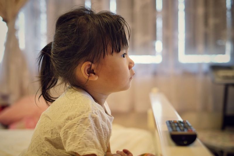 Side view of girl watching tv at home
