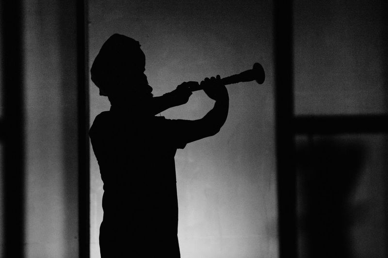 Silhouette man playing oboe by wall