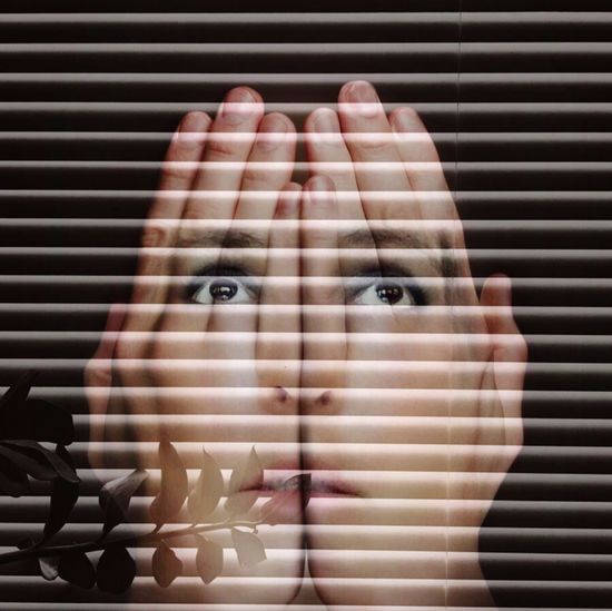 Double exposure of woman face with hands against blinds