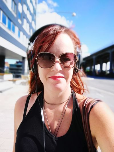 Close-up portrait of young woman wearing sunglasses and headphones on road