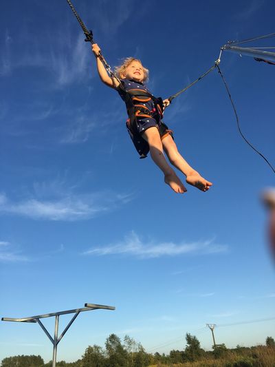 Low angle view of girl enjoying bungee jumping against blue sky