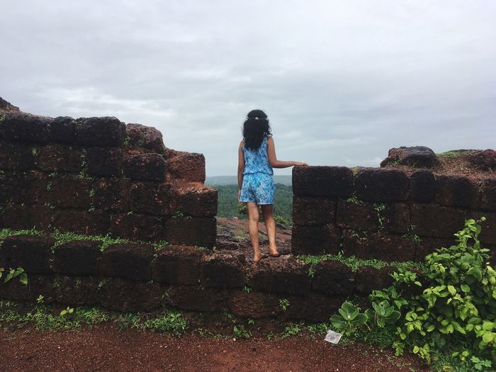 Rear view of girl standing on retaining wall against sky