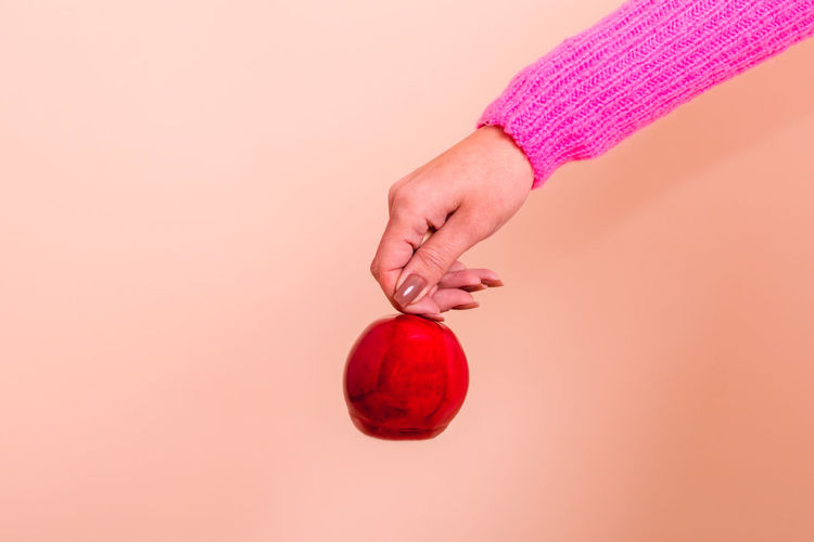 Cropped hand holding pumpkin against pink background