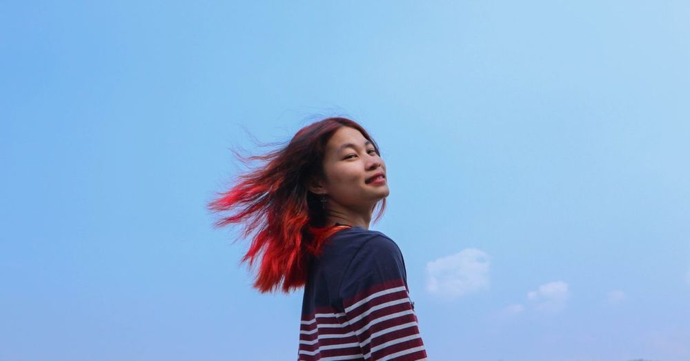 Portrait of beautiful young woman standing against blue sky