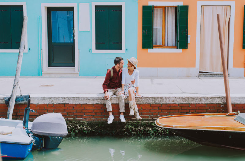 Young couple sitting by river against houses in city