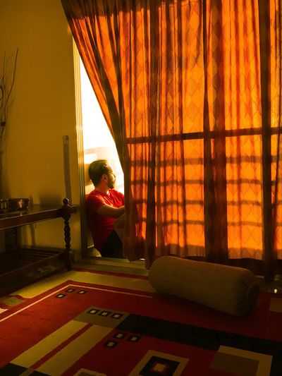 Young man looking through window while sitting at home