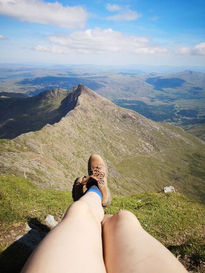 Low section of woman relaxing on mountain against sky