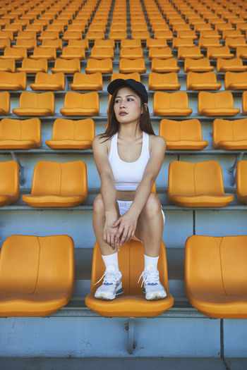 Confident asian athletic woman in sportswear sitting on stadium seat while resting after workout and looking away