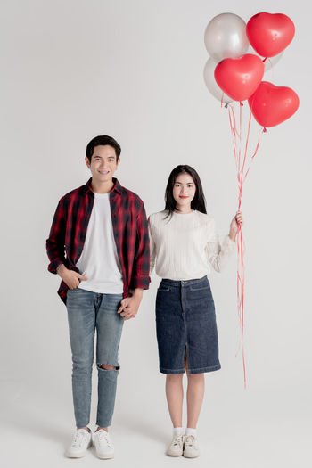Full length portrait of young couple standing against white background