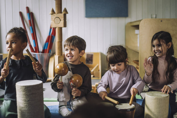 Multiracial male and female students enjoying while playing drum kit in kindergarten