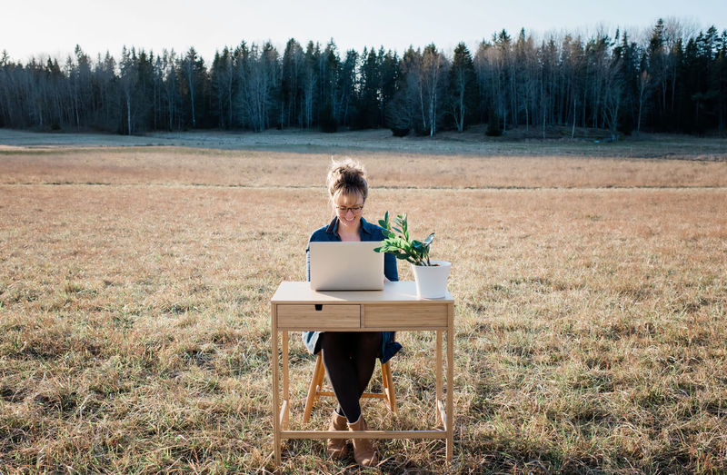 Travelling woman working on a laptop and desk in a field outside