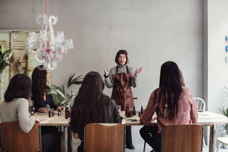 Confident female entrepreneur explaining to colleagues sitting at table in perfume workshop