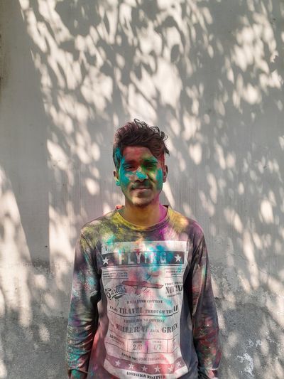 Portrait of young man with powder paint on face standing against wall