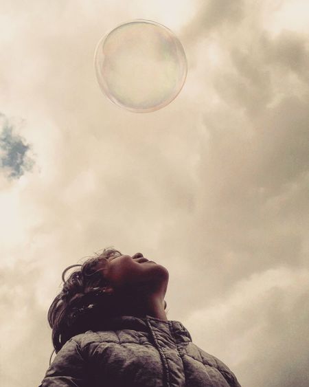 Low angle view of kid looking at bubbles against sky
