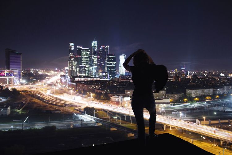 Silhouette woman standing on terrace against illuminated cityscape at night