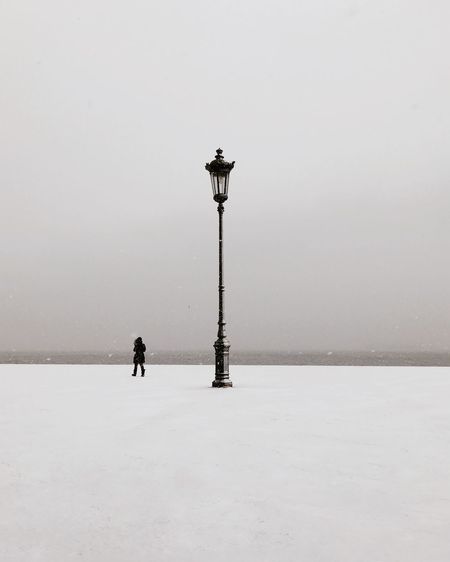 Person standing on snow covered street against sky during winter