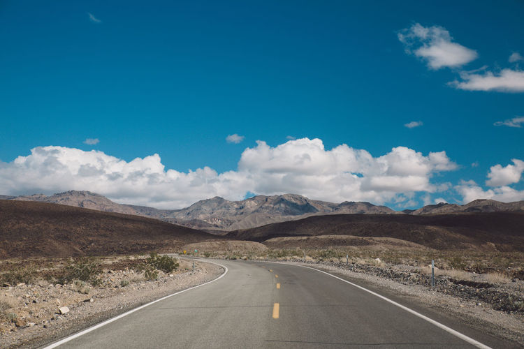 Empty road by mountains against blue sky