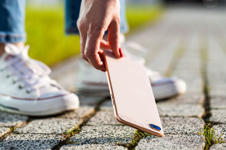 Low section of woman holding phone over footpath