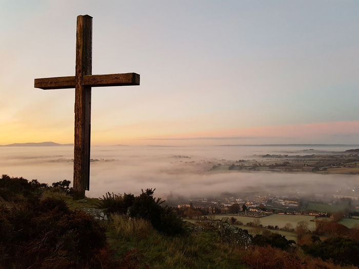 Cross on hill above mist covered rural town