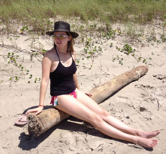 Semi-dressed young woman sitting on driftwood at beach during summer