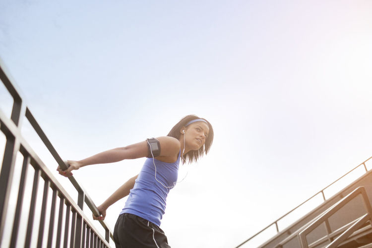 Low angle view of woman stretching on railing against clear sky