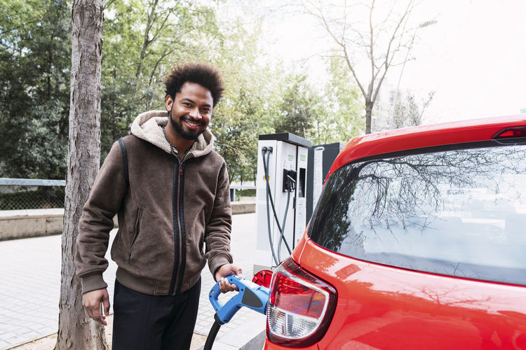 Smiling afro man charging red electric car at station