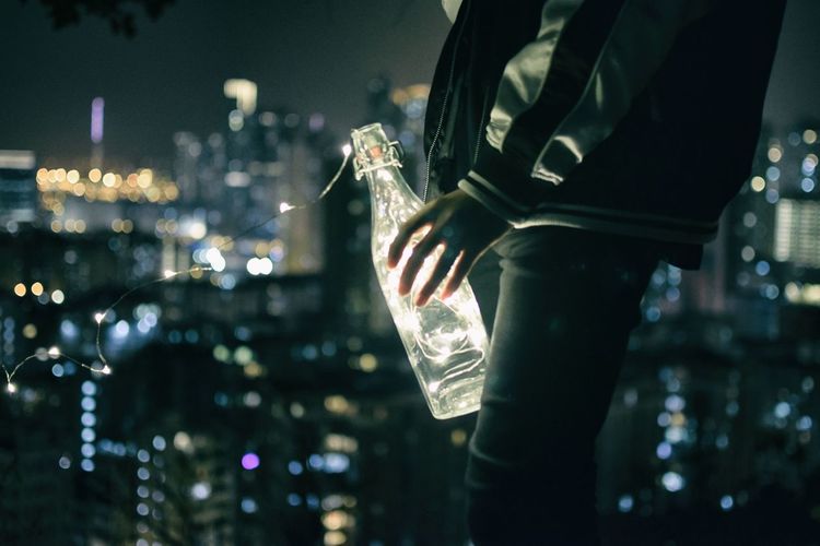 Close-up of hand holding illuminated bottle in city at night