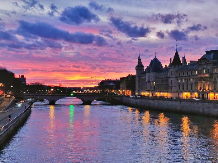 Bridge over river against buildings at sunset