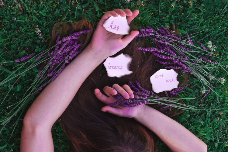 High angle view of woman holding flowers and labels while lying on field