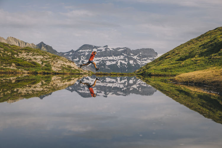 A hiker is jumping reflected in a mountain lake in chamonix valley.