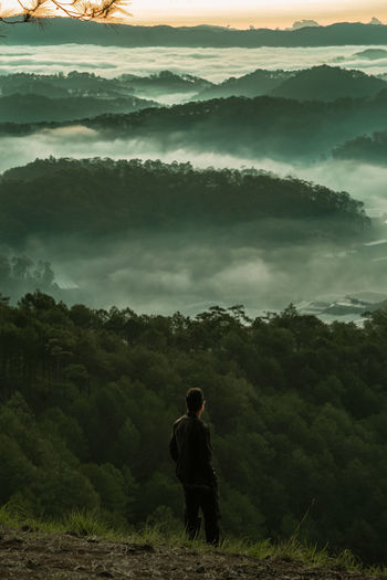 Rear view of man looking at mountain ranges with fog hover above the valley that against sky